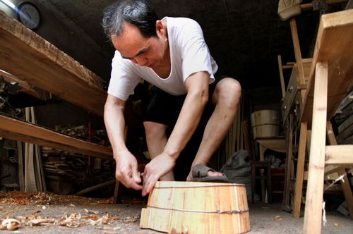 圆木匠余兴华在利用传统圆木制桶工艺制作圆形木制容器